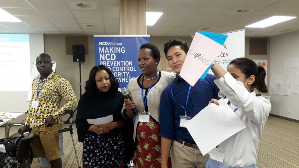People holding microphone and signs in front of NCD Alliance poster